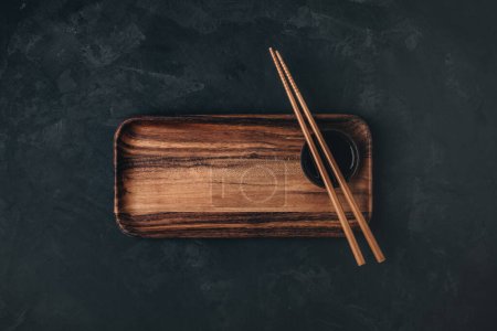 Photo for Empty wooden sushi plate with chopsticks on dark black stone background, top view - Royalty Free Image
