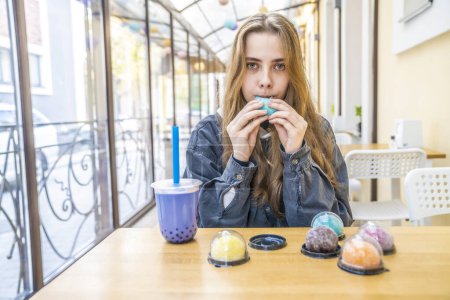 Téléchargez les photos : Fille aux cheveux bleus en pull bleu et écharpe noire avec tasse de café dans le café, bonbons, bonbons et bonbons - en image libre de droit