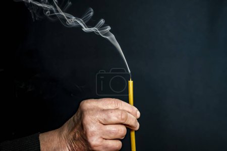 Photo for An elderly man, his hands are wrinkled. Holds a church candle, smoke. - Royalty Free Image