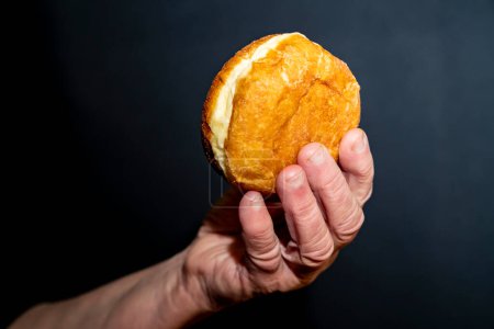 Foto de Un anciano tiene comida, un donut en sus manos. Fondo oscuro. - Imagen libre de derechos