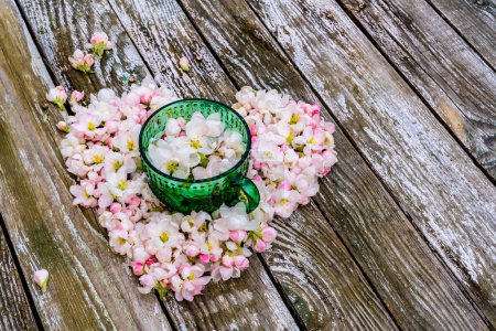 Foto de Corazón hecho de flores de primavera y taza verde sobre fondo de madera - Imagen libre de derechos