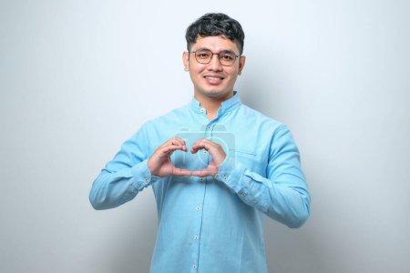 oung handsome man wearing casual shirt standing over isolated white background smiling in love doing heart symbol shape with hands. Romantic concept.