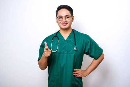 Photo for Confident smiling asian male doctor, nurse in scrubs pointing finger at camera, inviting for check-up or vaccination, give recommendation isolated over white background - Royalty Free Image