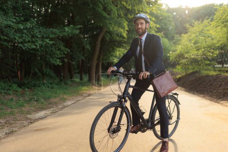 Foto de Elegant male entrepreneur in black suit, making stop, while riding on bicycle to work. Front view of positive bearded guy with bike taking rest, while commuting to job in morning. Concept of commute. - Imagen libre de derechos