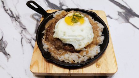 Photo for Burger steak patty with white rice and sunny side up egg served in black cooking pan - Royalty Free Image