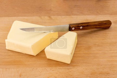 Photo for Block of butter cut with wooden handled knife on wooden cutting board - Royalty Free Image