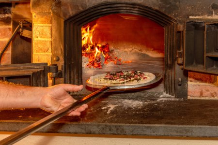 Téléchargez les photos : Main de pizzailo met la pizza sur une pelle dans le four traditionnel au bois. - en image libre de droit