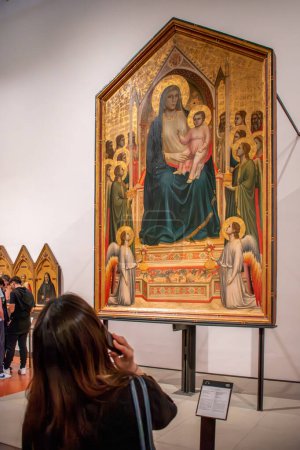 Photo for Florence, Italy - April 04, 2024: Female visitor listens to audio guide while observing Giotto's work Madonna Enthroned with Child among Angels and Saints ( 14th century) displayed in the Uffizi Gallery in Florence - Royalty Free Image