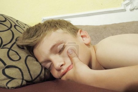 Foto de Un chico caucásico de 10 años se durmió en el sofá. Los niños sueñan. Problemas para dormir, quedarse dormido, insomnio, fatiga. El concepto de salud, modo de vigilia y descanso, educación y prevención - Imagen libre de derechos