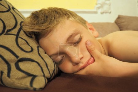 Foto de Un chico caucásico de 10 años se durmió en el sofá. Los niños sueñan. Problemas para dormir, quedarse dormido, insomnio, fatiga. El concepto de salud, modo de vigilia y descanso, educación y prevención - Imagen libre de derechos