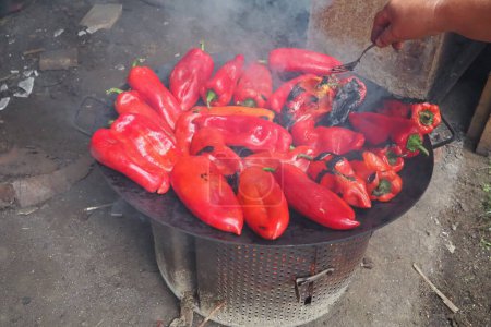 Photo for Roasting red peppers for a smoky flavor and quick peeling. Thermal processing of the pepper crop on metal circle. Brazier container used to burn charcoal fuel for cooking, heating or cultural rituals - Royalty Free Image
