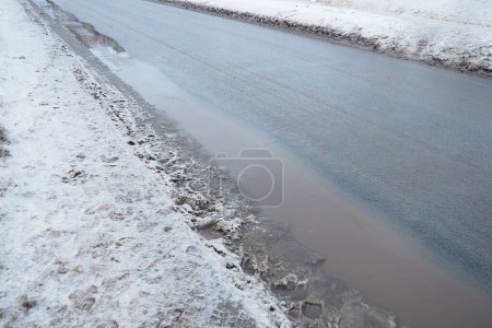 Photo for Ice on city roads. Wet asphalt with sand. Snow-covered roadsides. Weather forecast. Thaw in winter. Snow melting. The air temperature is near zero. Footprints of people. Difficult driving conditions - Royalty Free Image