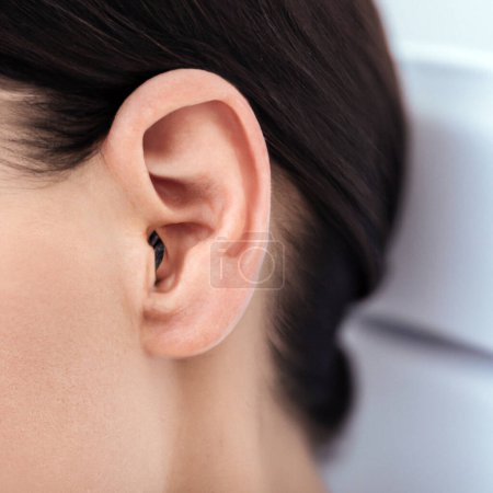 Foto de Ear and part of the cheek on the head of a brunette woman close-up. Dark hair is slicked back and pinned up with barrette. Ear without earring. Surdology, otolaryngology. Turning the head to the side. - Imagen libre de derechos
