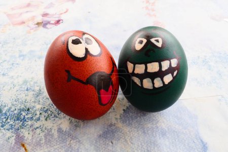 Photo for Easter eggs dyed green and brown with painted laughing faces. Funny grimaces with eyes, tongue and big white teeth. Scary face for Halloween. Emoticon for Easter. Light abstract background - Royalty Free Image