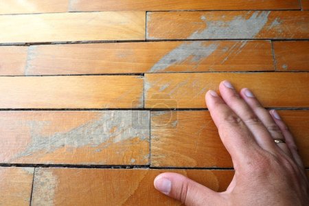 Old, scratched parquet flooring needs maintenance. the parquet is damaged by scratches from prolonged use. Masters hands show damage to the floor.