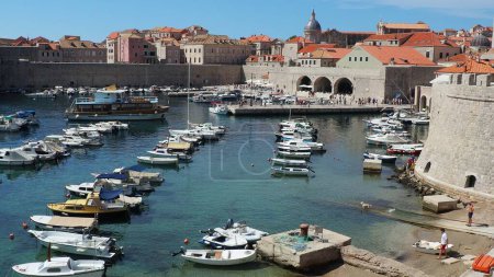 Photo for Dubrovnik, Croatia, August 14, 2022. City port in summer, tourist attraction. Tourists walk, get into boats and ships and go on boat trips. Adriatic Sea. A local resident plays with a dog. Old forts - Royalty Free Image