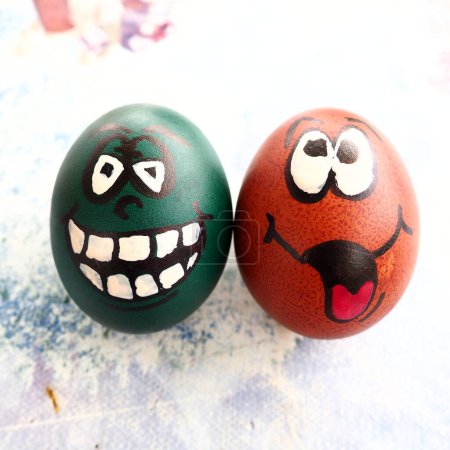 Photo for Easter eggs dyed green and brown with painted laughing faces. Funny grimaces with eyes, tongue and big white teeth. Scary face for Halloween. Emoticon for Easter. Light abstract background - Royalty Free Image