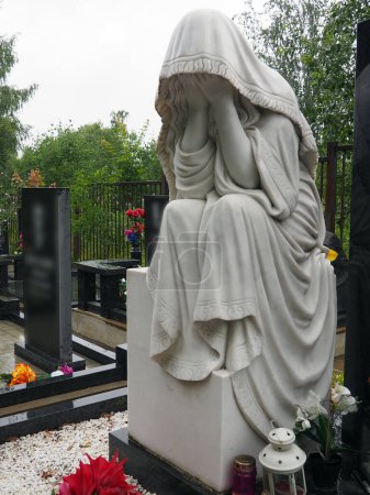 Weeping woman. Sculpture in the cemetery. The figure of a mother, wife or woman in a hood or stole. Lamentation for the deceased. Tombstone on a Christian grave. Sadness and grief.