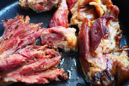 Roasted smoked pork shoulder or knee. Delicious meat on a black baking sheet with drops of vegetable oil, taken out of the oven. Pork delicacy for dinner in a restaurant and family lunch. Red meat.