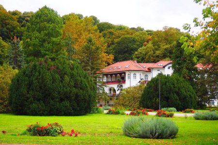 Foto de Banja Koviljaca, Serbia, Guchevo, Loznica, 30 de septiembre de 2022 Un edificio médico, la antigua villa real. Césped verde en el parque con flores y arbustos. Paisajismo y decoración de la zona del parque - Imagen libre de derechos