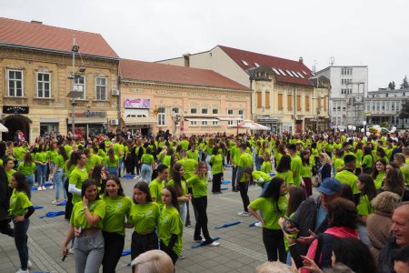 Foto de Sremska Mitrovica, Serbia, 19 de mayo de 2023 Bola de graduados de escuelas y escuelas técnicas en la plaza central. La juventud realiza una danza colectiva. Las niñas y los niños usan camisetas verdes. Día de graduación. - Imagen libre de derechos