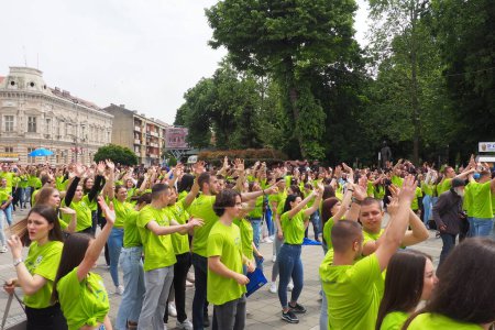 Foto de Sremska Mitrovica, Serbia, 19 de mayo de 2023 Bola de graduados de escuelas y escuelas técnicas en la plaza central. La juventud realiza una danza colectiva. Las niñas y los niños usan camisetas verdes. Día de graduación. - Imagen libre de derechos