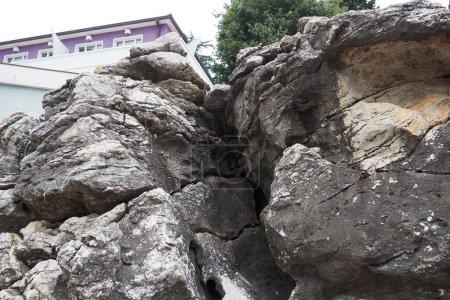 Foto de Casa hotel en el borde de una roca, lava volcánica endurecida. Herceg Novi, Montenegro. Una gran grieta en la roca, una cueva. Capas en una roca. Geología y sismología en la región del Adriático Mediterráneo. - Imagen libre de derechos