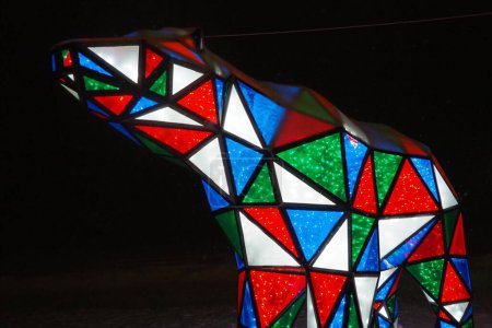 Photo for Bear garland. Multi-colored sparkling electric New Year Christmas bear on snow at night. Installation figure, architectural form for decorating streets on holiday. Red, blue, green, white triangle. - Royalty Free Image