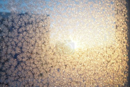 Photo for The frosty pattern on window glass occurs due to the condensation of water vapor on glass cooled below 0 degree. Frost flowers, curls and crystals. Morning yellow-orange low winter sun on the horizon. - Royalty Free Image