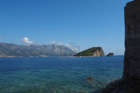 Budva Montenegro. Hermoso día de verano en el mar Adriático. La isla de Sveti Nikola se encuentra frente al casco antiguo de Budva. Un acantilado que se eleva 121 metros. Los barcos navegan en el agua. Olas y rocas de mar salado.