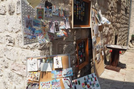 Photo for Kotor, Montenegro, August 11, 2022: souvenir cards, drawings, pictures and magnets are hung on the wall and on a metal sign. Tourist walks around the old town. Sea summer breeze. Ancient stone walls - Royalty Free Image