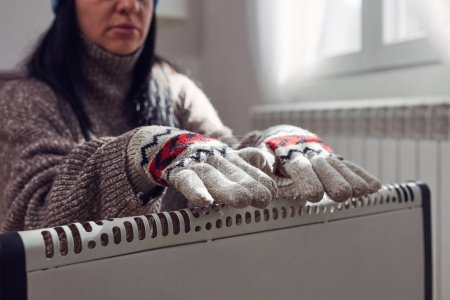Téléchargez les photos : Femme veste, pull et gants de main à l'intérieur par une journée froide d'hiver, crise de l'énergie et du gaz, chambre froide, problèmes de chauffage. - en image libre de droit