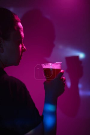 Téléchargez les photos : Femme tenant et buvant une tasse de bière en plastique dans la boîte de nuit. - en image libre de droit