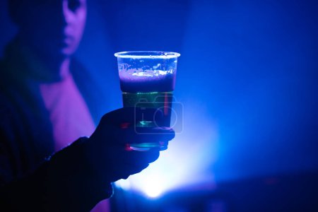 Téléchargez les photos : Personne tenant une tasse de bière en plastique dans la boîte de nuit. - en image libre de droit