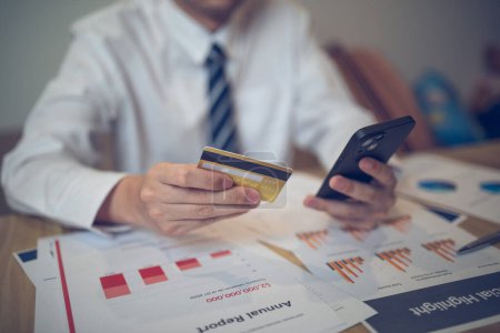 Empresario sosteniendo una tarjeta de crédito y un teléfono inteligente en medio de papeles financieros. Concepto de negocio de comercio electrónico.