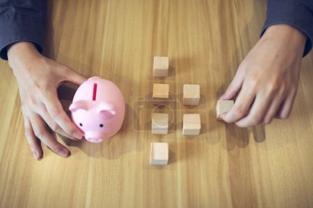 A person with a piggy bank and wooden blocks on a table, illustrating concepts of savings and investment.