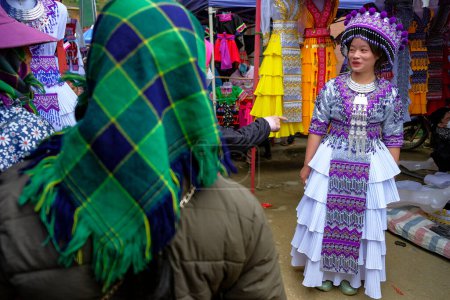 Téléchargez les photos : Can Cau, Vietnam - 17 décembre 2022 : Une femme essaie une robe traditionnelle sur le marché de Can Cau dans la province de Lao Cai, Vietnam. - en image libre de droit