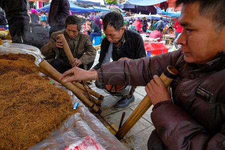 Téléchargez les photos : Bac Ha, Vietnam - décembre 18, 2022 : Hommes fumant du tabac au marché hebdomadaire Bac Ha au Vietnam. - en image libre de droit