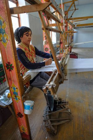 Foto de Margilan, Uzbekistán - 20 de octubre de 2023: Una mujer que trabaja con seda en un telar en Margilan, Uzbekistán. - Imagen libre de derechos