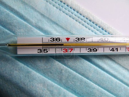 Téléchargez les photos : Thermomètre au mercure médical montre la température normale : 36,6 degrés sur le fond d'un masque de protection médicale - en image libre de droit