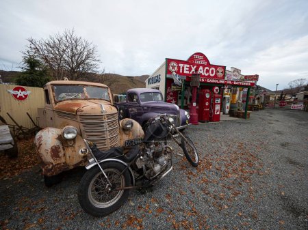 Photo for Burkes Pass Village, Canterbury, South Island, New Zealand - 2023: Old motorbike and rusty classic cars infront of Texaco historic antique gas station fuel pump - Royalty Free Image