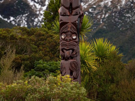 Detailed closeup of typical traditional Pou Whenua wooden pole Whakairo carvings from Maori culture with plants background at Dawson Falls Taranaki North Island New Zealand