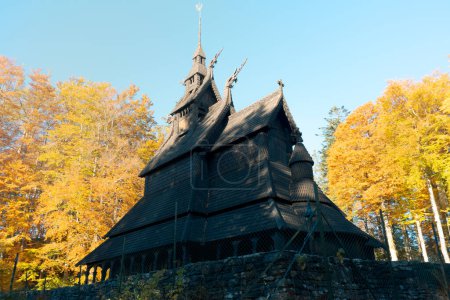 Téléchargez les photos : Image horizontale de l'église en bois de Fantoft à Bergen. Dans les arbres de fond dans les couleurs d'automne avec un ciel bleu clair. Vacances en Norvège. - en image libre de droit
