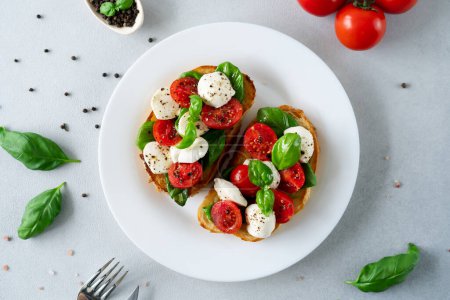 Photo for Top view of Bruschetta with tomatoes, mozzarella and basil leaves on light background. Crostino Caprese - Royalty Free Image