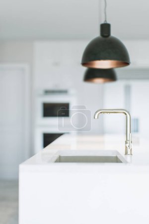 Foto de Una imagen de una cocina blanca con electrodomésticos, luminarias y una vista del fregadero y el grifo. El fondo está borroso, el foco está en el grifo de la cocina. Renderizado 3D. - Imagen libre de derechos