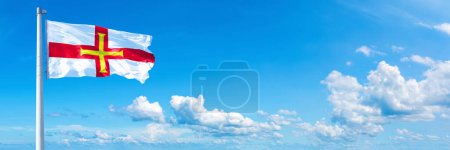 Foto de Guernsey Flag - state of Europe, flag waving on a blue sky in beautiful clouds - Horizontal banner - Imagen libre de derechos