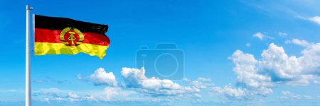 Téléchargez les photos : Allemagne de l'Est Drapeau - drapeau historique de l'Allemagne, drapeau agitant sur un ciel bleu dans de beaux nuages - Bannière horizontale - en image libre de droit