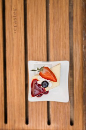 Foto de Pieza de pastel de queso con mermelada de mora y un pedazo de fresa cortado mas una arandano vertical - Imagen libre de derechos