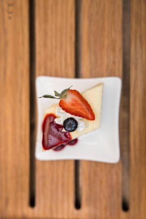 Photo for Pedazo de pastel de queso con mermelada de mora y un pedazo de fresa cortado mas una arandano en vertical - Royalty Free Image
