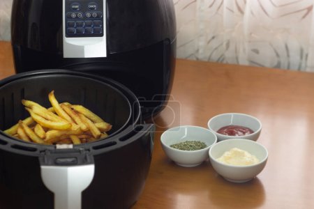 Air fryer with French fries on a table with sauces and spices. healthy food concept
